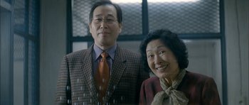 Movie still from “Mother” (2009), directed by Bong Joon Ho – An older man standing next to an older woman; Medium shot, Low angle