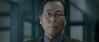 Movie still from “Mother” (2009), directed by Bong Joon Ho – An older man wearing glasses and a suit; Close Up shot, Low angle