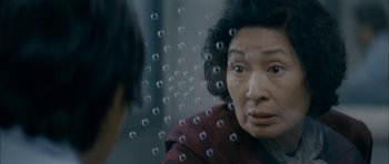 Movie still from “Mother” (2009), directed by Bong Joon Ho – An older asian woman looking out of a glass window; Close Up shot, Over the shoulder angle