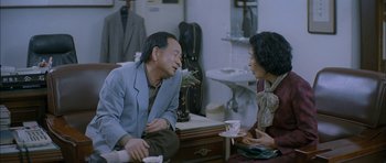 Movie still from “Mother” (2009), directed by Bong Joon Ho – A man and a woman sitting in a living room talking to each other; Medium shot, Over the shoulder angle