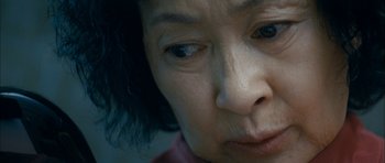 Movie still from “Mother” (2009), directed by Bong Joon Ho – An older asian woman with blue eyes looking sad; Extreme Close Up shot, High angle
