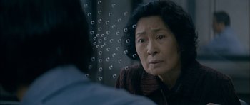 Movie still from “Mother” (2009), directed by Bong Joon Ho – An older asian woman looking out of a window; Close Up shot, Over the shoulder angle