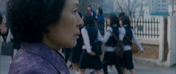 Movie still from “Mother” (2009), directed by Bong Joon Ho – An asian woman looking at a group of people; Close Up shot, Over the shoulder angle