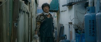 Movie still from “Mother” (2009), directed by Bong Joon Ho – An asian man in an alleyway holding a shovel; Medium shot, Low angle