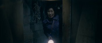 Movie still from “Mother” (2009), directed by Bong Joon Ho – An older woman holding a flashlight in a doorway; Medium shot, High angle