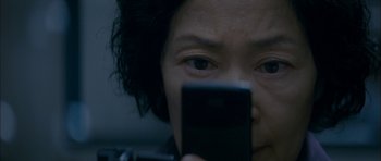 Movie still from “Mother” (2009), directed by Bong Joon Ho – A woman looking at a cell phone while sitting in a car; Extreme Close Up shot, High angle