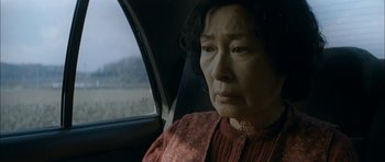 Movie still from “Mother” (2009), directed by Bong Joon Ho – An older woman sitting in the back seat of a car; Close Up shot, High angle