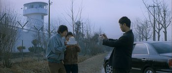 Movie still from “Mother” (2009), directed by Bong Joon Ho – A man taking a picture of two people holding a cake; Wide shot, Over the shoulder angle