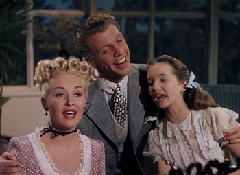 Movie still from “Mother Wore Tights” (1947), directed by Walter Lang – A man and two young girls are posing for a picture; Medium shot, Low angle