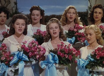 Movie still from “Mother Wore Tights” (1947), directed by Walter Lang – A group of young women standing next to each other holding pink roses; Medium shot, Low angle
