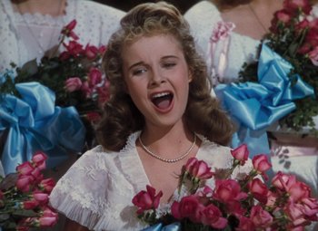 Movie still from “Mother Wore Tights” (1947), directed by Walter Lang – A young girl in a white dress with a bunch of pink flowers; Close Up shot, Low angle