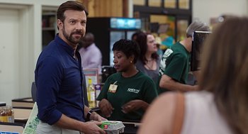 Movie still from “Mother's Day” (2016), directed by Garry Marshall – A man standing in front of a counter holding a box; Medium shot, Over the shoulder angle