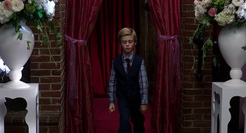 Movie still from “Mother's Day” (2016), directed by Garry Marshall – A young boy in a suit and tie walking through a doorway; Wide shot, High angle