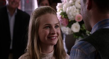Movie still from “Mother's Day” (2016), directed by Garry Marshall – A young woman smiles brightly while sitting in front of flowers; Close Up shot, Over the shoulder angle