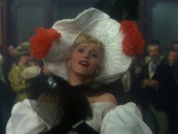 Movie still from “Moulin Rouge” (1952), directed by John Huston – A woman wearing a white hat with red feathers on top of her head; Medium shot, Low angle