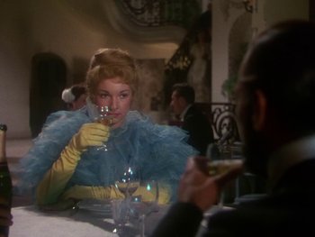 Movie still from “Moulin Rouge” (1952), directed by John Huston – A woman in a yellow and blue dress drinking wine; Medium shot, Over the shoulder angle