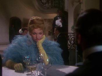 Movie still from “Moulin Rouge” (1952), directed by John Huston – A woman sitting at a table with a glass of wine in front of her; Medium shot, Over the shoulder angle