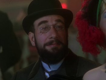 Movie still from “Moulin Rouge” (1952), directed by John Huston – A man with a beard wearing glasses and a hat; Close Up shot, Over the shoulder angle