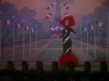Movie still from “Moulin Rouge” (1952), directed by John Huston – A woman in a red and black dress in front of a painting of the eiffel tower; Wide shot, Low angle
