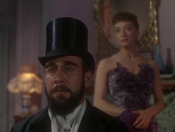 Movie still from “Moulin Rouge” (1952), directed by John Huston – A man in a top hat and glasses in front of a woman in a purple dress; Close Up shot, Over the shoulder angle