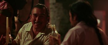 Movie still from “Mr. & Mrs. Smith” (2005), directed by Doug Liman – A man smiling while sitting next to another man holding a bottle; Close Up shot, Over the shoulder angle