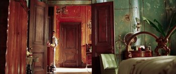 Movie still from “Mr. & Mrs. Smith” (2005), directed by Doug Liman – A room with two wooden doors and a green chair; Wide shot, Low angle