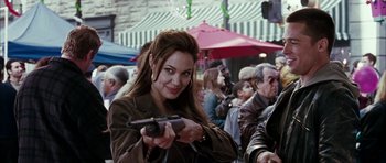Movie still from “Mr. & Mrs. Smith” (2005), directed by Doug Liman – A beautiful woman holding a gun while standing in front of a crowd of onlookers; Medium shot, Over the shoulder angle