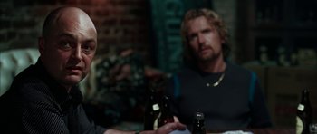 Movie still from “Mr. & Mrs. Smith” (2005), directed by Doug Liman – Two men sitting at a table with a bottle of beer in front of them; Medium shot, Over the shoulder angle