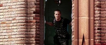 Movie still from “Mr. & Mrs. Smith” (2005), directed by Doug Liman – A man in a leather vest standing in front of a brick wall; Medium shot, Low angle