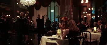 Movie still from “Mr. & Mrs. Smith” (2005), directed by Doug Liman – A woman sitting at a table with a glass of wine; Wide shot, Over the shoulder angle