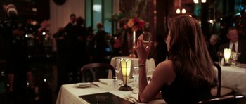 Movie still from “Mr. & Mrs. Smith” (2005), directed by Doug Liman – A woman sitting at a table holding a glass of wine; Medium shot, Over the shoulder angle
