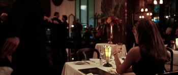 Movie still from “Mr. & Mrs. Smith” (2005), directed by Doug Liman – A woman sitting at a table with a glass of wine; Medium shot, Over the shoulder angle