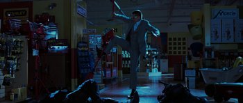 Movie still from “Mr. & Mrs. Smith” (2005), directed by Doug Liman – A man in a business suit is kicking a skateboard in a store; Wide shot, Low angle