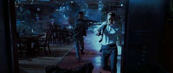 Movie still from “Mr. & Mrs. Smith” (2005), directed by Doug Liman – Two men in suits are holding guns in a room; Wide shot, Over the shoulder angle