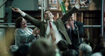 Movie still from “Mr. Bean's Holiday” (2007), directed by Steve Bendelack – A man in a suit and red tie raising his arms in the air; Medium shot, Low angle