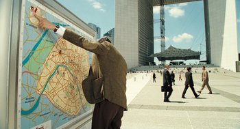 Movie still from “Mr. Bean's Holiday” (2007), directed by Steve Bendelack – A man pointing to a map on the side of a building; Wide shot, High angle