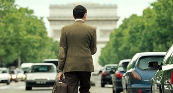 Movie still from “Mr. Bean's Holiday” (2007), directed by Steve Bendelack – A man in a brown suit is holding a briefcase; Wide shot, Over the shoulder angle