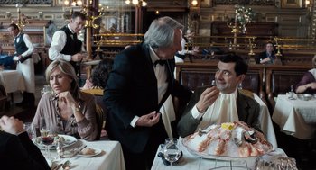 Movie still from “Mr. Bean's Holiday” (2007), directed by Steve Bendelack – Two men in suits and ties at a table with food; Medium shot, Over the shoulder angle