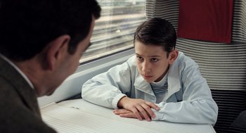 Movie still from “Mr. Bean's Holiday” (2007), directed by Steve Bendelack – A young boy sitting in front of a window with his hand on his chin; Medium shot, High angle