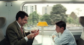 Movie still from “Mr. Bean's Holiday” (2007), directed by Steve Bendelack – A man and a young boy sitting on a train; Medium shot, Over the shoulder angle