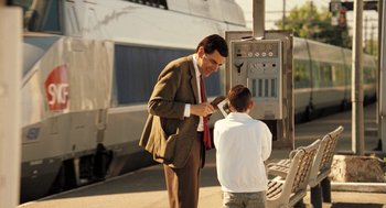 Movie still from “Mr. Bean's Holiday” (2007), directed by Steve Bendelack – A man and a boy standing next to each other near a train; Medium shot, Over the shoulder angle