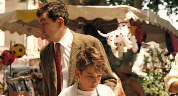 Movie still from “Mr. Bean's Holiday” (2007), directed by Steve Bendelack – A man standing next to a woman in a suit; Medium shot, Over the shoulder angle