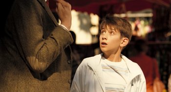 Movie still from “Mr. Bean's Holiday” (2007), directed by Steve Bendelack – A young boy standing next to an older man; Medium shot, Over the shoulder angle