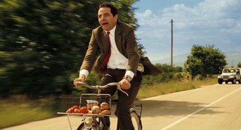 Movie still from “Mr. Bean's Holiday” (2007), directed by Steve Bendelack – A man riding a bike with a basket full of fruit; Medium shot, Low angle