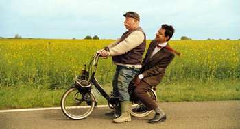 Movie still from “Mr. Bean's Holiday” (2007), directed by Steve Bendelack – Two men riding a bicycle on a road; Wide shot, Low angle