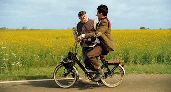 Movie still from “Mr. Bean's Holiday” (2007), directed by Steve Bendelack – Two men riding a bicycle on the side of the road; Wide shot, Low angle