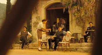 Movie still from “Mr. Bean's Holiday” (2007), directed by Steve Bendelack – A man sitting at an outdoor table with a woman; Wide shot, High angle