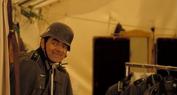 Movie still from “Mr. Bean's Holiday” (2007), directed by Steve Bendelack – A man wearing a german helmet in front of a tent; Close Up shot, Over the shoulder angle