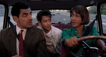Movie still from “Mr. Bean's Holiday” (2007), directed by Steve Bendelack – A group of people riding in the back of a car; Medium shot, Over the shoulder angle