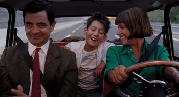 Movie still from “Mr. Bean's Holiday” (2007), directed by Steve Bendelack – A group of people sitting in the back of a car; Medium shot, Over the shoulder angle
